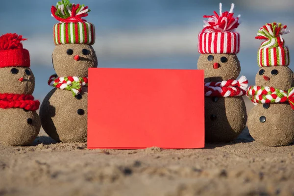 Família de bonecos de neve arenosos na praia tropical com cartão em branco . — Fotografia de Stock