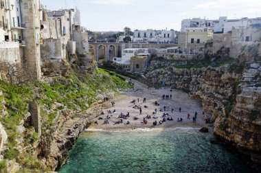 Polignano A Mare, İtalya - 29 Mart 2018: İnsanlar kayalıklarla Adriyatik Denizi Polignano içinde yükselen bir Mare, Puglia, İtalya mağaralar ile dramatik manzaralı güzel plajda Lama Monachile