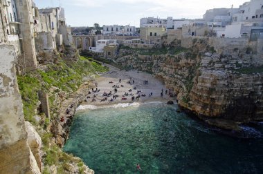 Polignano A Mare, İtalya - 29 Mart 2018: İnsanlar kayalıklarla Adriyatik Denizi Polignano içinde yükselen bir Mare, Puglia, İtalya mağaralar ile dramatik manzaralı güzel plajda Lama Monachile