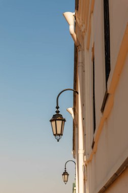 Mavi gökyüzünün arka planına karşı eski kilise duvarının beyaz taş duvarında eski fenerler, dikey görüntü