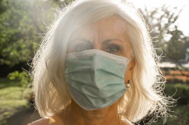 Cerrahi maske takan orta yaşlı güzel bir kadın akşam vakti parkta yürür.