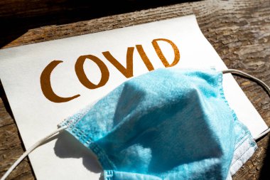 Üzerinde mavi koruyucu tıbbi maske olan altın renkli covid-19 yazıtların yakın çekimi. Covid-19 'un yayılmasına karşı koruyucu önlemler