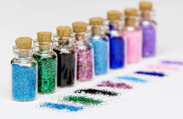 Pequenas garrafas com brilhos multicoloridos e lantejoulas espalhadas no fundo branco — Fotografia de Stock