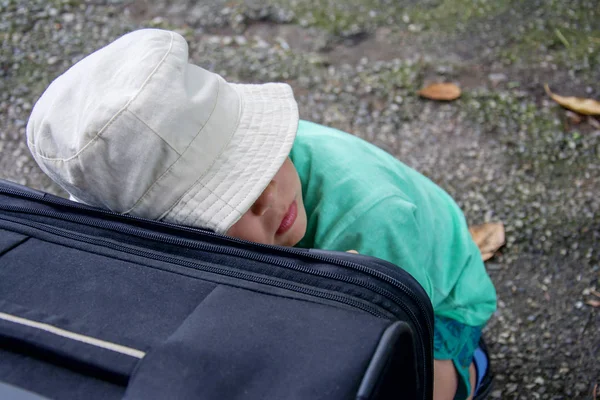 帽子をかぶった少年が眠っていると旅の列車を待っているスーツケースに対して身を乗り出して — ストック写真