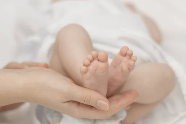 As mãos da mãe seguram suavemente os pés de um bebê recém-nascido nas palmas das mãos — Fotografia de Stock