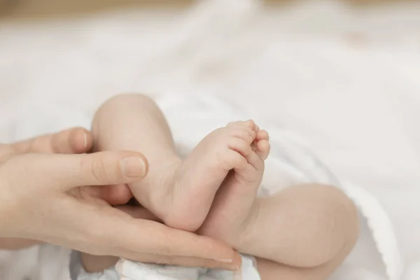 As mãos da mãe seguram suavemente os pés de um bebê recém-nascido nas palmas das mãos — Fotografia de Stock