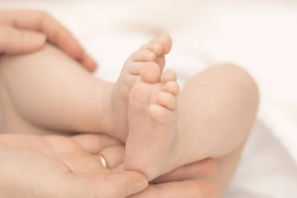 As mãos da mãe seguram suavemente os pés de um bebê recém-nascido nas palmas das mãos — Fotografia de Stock