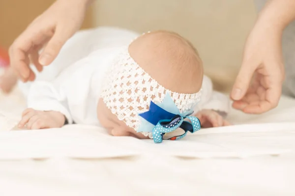 A beautiful baby girl lying on her stomach raises her head, and her mother's hands help her — Stock Photo, Image