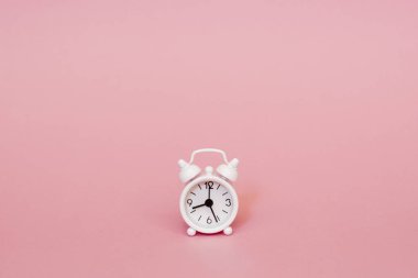 Küçük beyaz küçük çalar saat pembe bir arka plan üzerinde. minimalizm