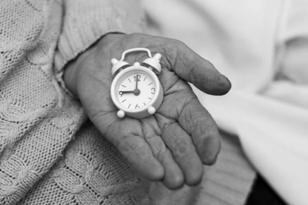 Die Hand des alten Mannes hält eine kleine weiße Uhr in der Hand — Stockfoto