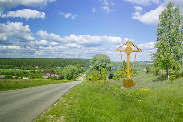 Cross on the side of the road in front of the Russian village as a talisman on the mountain