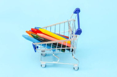 balmumu renkli kalemler ile mavi bir arka plan üzerinde metal bir alışveriş sepeti küçük bir kopyası. okula dönüş. kopya alanı