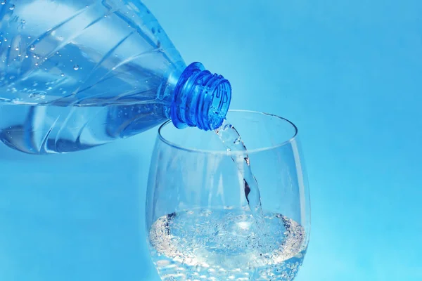 clean, clear cool mineral water is poured from a plastic bottle into a clear glass glass goblet