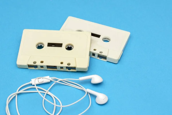 technology - old retro cassette tapes and new modern white headphones on blue background