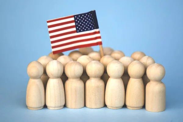Persone senza volto in legno in piedi tra la folla con una bandiera americana sollevata su uno sfondo di luce blu . — Foto Stock