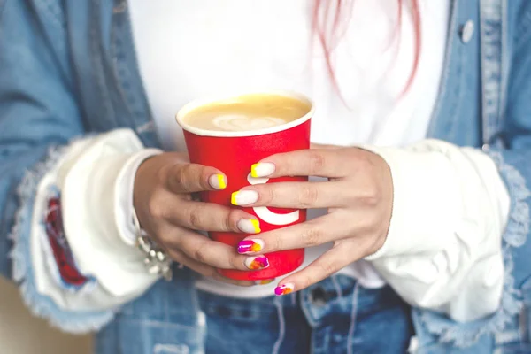 Χέρια κορίτσια με φωτεινό καλοκαιρινό μανικιούρ κρατώντας ένα κόκκινο φλιτζάνι καφέ με μια βαμμένη καρδιά. Εικόνα Αρχείου