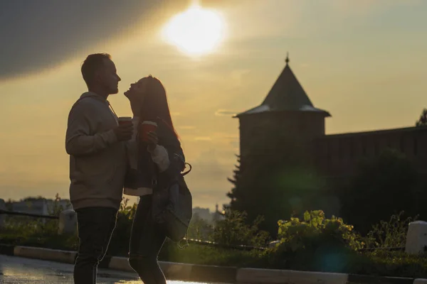 La pareja joven - la muchacha y el muchacho la puesta del sol el fondo veraniego del cielo. Siluetas y sombras de las personas . — Foto de Stock