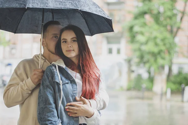 Pareja joven enamorada feliz bajo un paraguas bajo la lluvia en el verano . — Foto de Stock