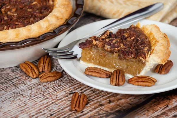 A slice of homemade pecan pie with pecans on rustic wooden table