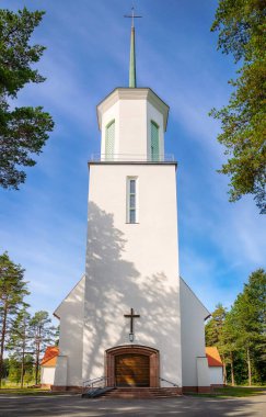 Facade of a beautiful white Lutheran church in rural Finland. Bright blue sky and trees background.