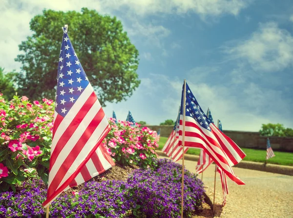 7月4日には道路脇にアメリカ国旗が掲揚された 美しい花壇と青空の背景 — ストック写真