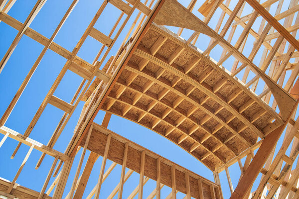 New construction home framing against blue sky. Ceiling frame and arch structure details.