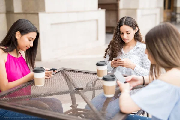 三多名女孩在街头咖啡馆喝咖啡 并更新智能手机的社交媒体地位 — 图库照片