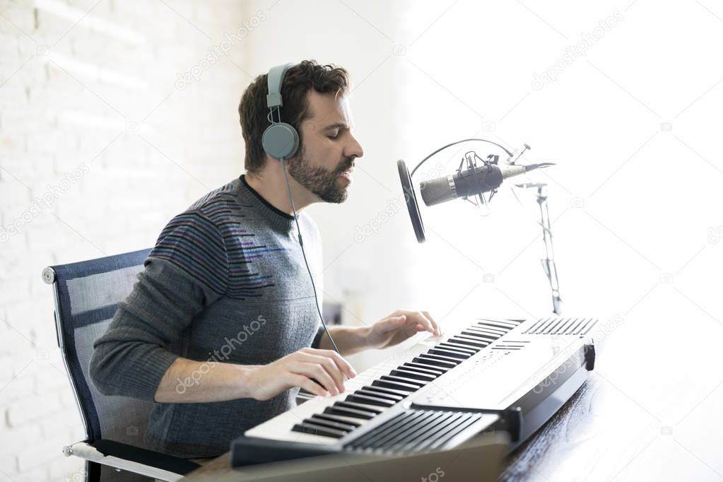 Profile view of good looking latin man with headphones playing piano and singing into a mic, singing over online radio show.