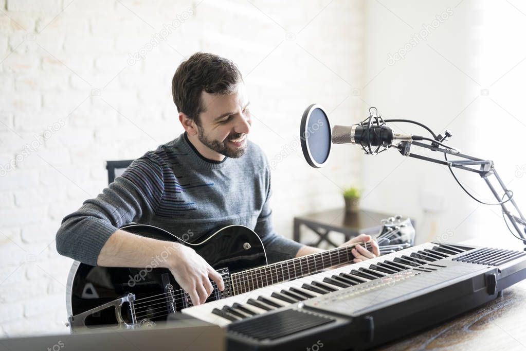 Handsome hispanic man enjoying playing guitar at radio station, playing music live on air and smiling.