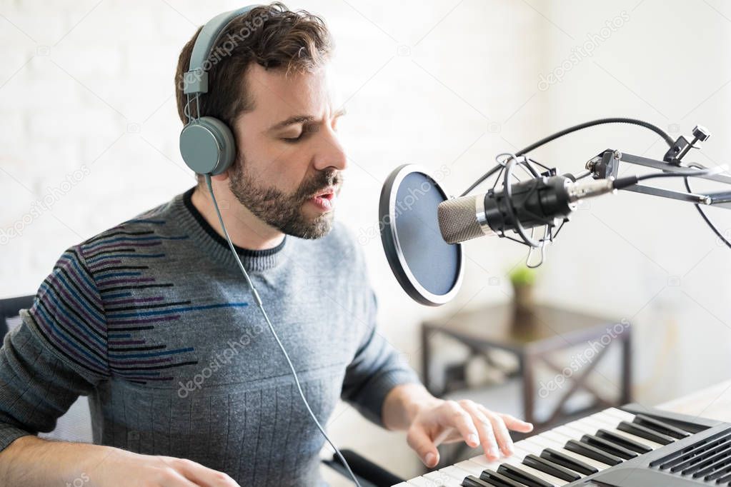 Good looking latin man singer with headphones singing a song and playing piano into mic at radio station