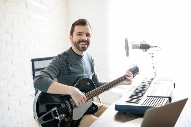 Radyo istasyonunda bir göz teması yapma gitar ile oturan genç adam gülümseyen