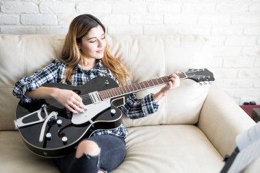 Oturma odasında kanepede rahatlatıcı ve gitar çalmak genç ve güzel beyaz kadın müzisyen