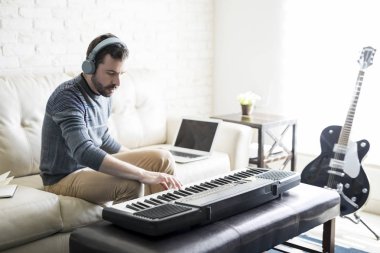 Müzik ve evde oturma odasında otururken elektrikli piyano ile bir şarkı bestelemek yakışıklı delikanlı