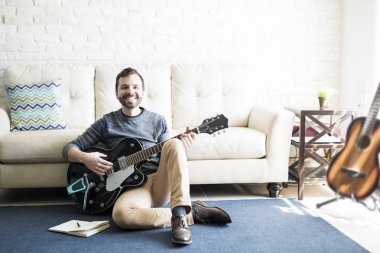 Bir kitap ve gitar ile katta oturan gülümseyen erkek müzik bestecisi