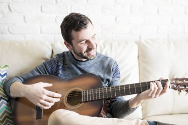 Bir gitar çalmak ve evde gülümseyen yakışıklı genç latin adam portresi