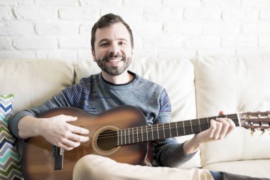 Bir gitar ile kanepede oturan ve bir göz teması yapma iyi görünümlü genç İspanyol adam portresi