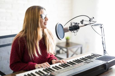 Portrait of woman singer playing electric piano and singing a song into mic on online radio clipart