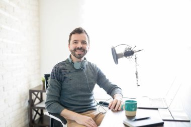 Dizüstü bilgisayar ve mikrofon onun masasına oturan iyi görünümlü genç İspanyol bir adam portresi