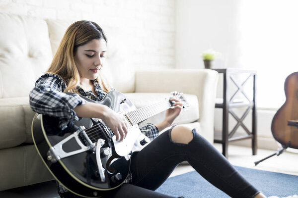 Beautiful young woman in her 20s sitting in living room with her guitar and thinking of new tune for her song