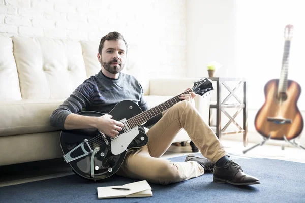 ノートが付いている床の上に座って ギターを弾く男性のソング ライターの肖像画 — ストック写真