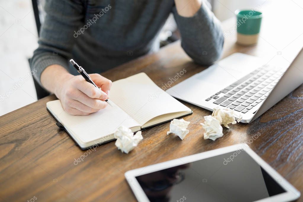 Close up of male author writing a book with crumpled pages on table