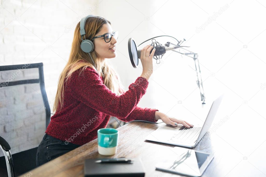 Profile view of beautiful young woman sitting at a table with laptop talking into microphone