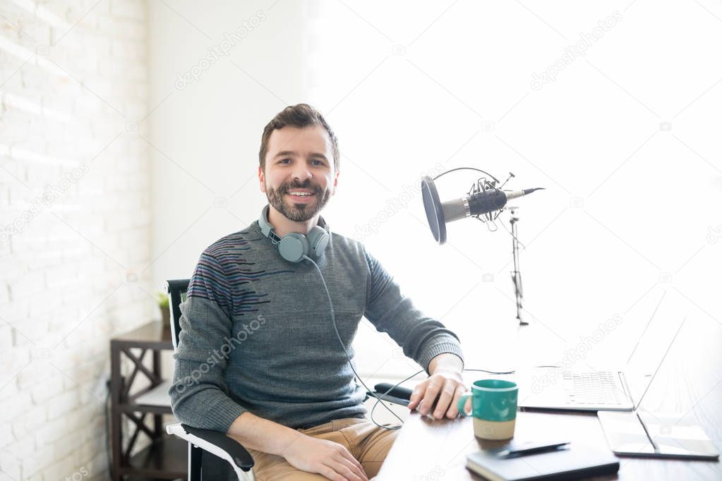 Portrait of good looking young hispanic man sitting his desk with laptop and microphone