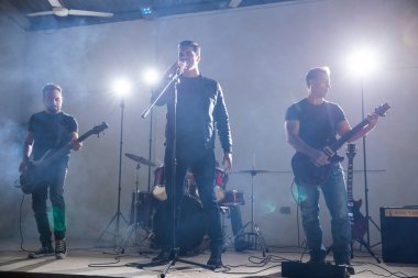 Grup dört müzisyen sahne ışıkları ve çevresinde duman ile müzik çalma