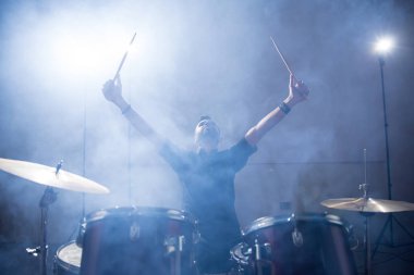 Işık ve duman ile sahnede kollarını yükselterek rock band davulcu