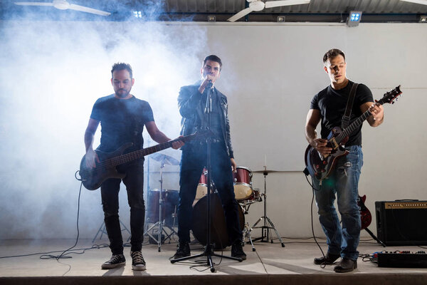 Rock and roll music band performing on stage with lights and smoke at the back