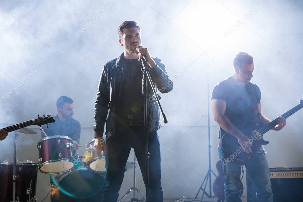 Rock band playing live on stage during a music concert with bright lights and smoke around