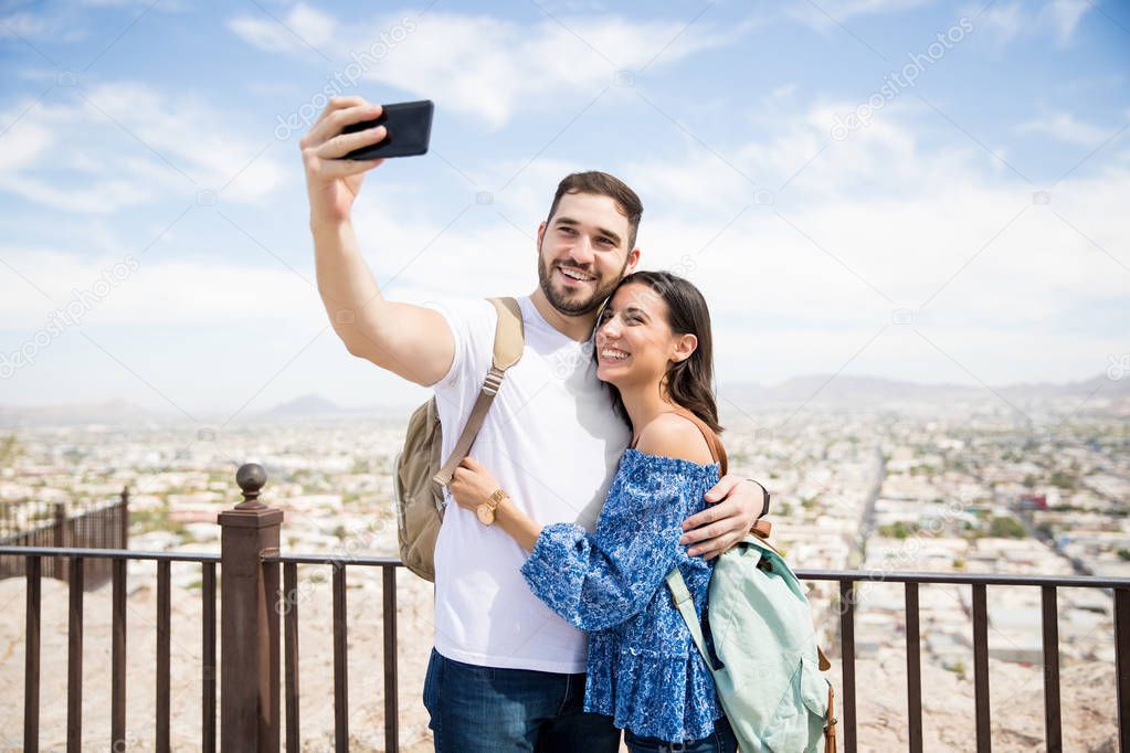 Happy young man and woman taking self portrait with city scenery in background during day