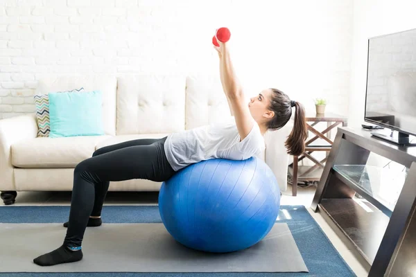 安定性のボール上に傾いて 重みを持つ手のトレーニングをやってフィットの若いのヒスパニック系の女性 — ストック写真