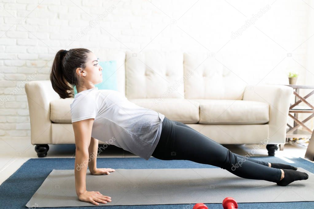 Profile view of fit young woman doing stretches on exercise mat at home
